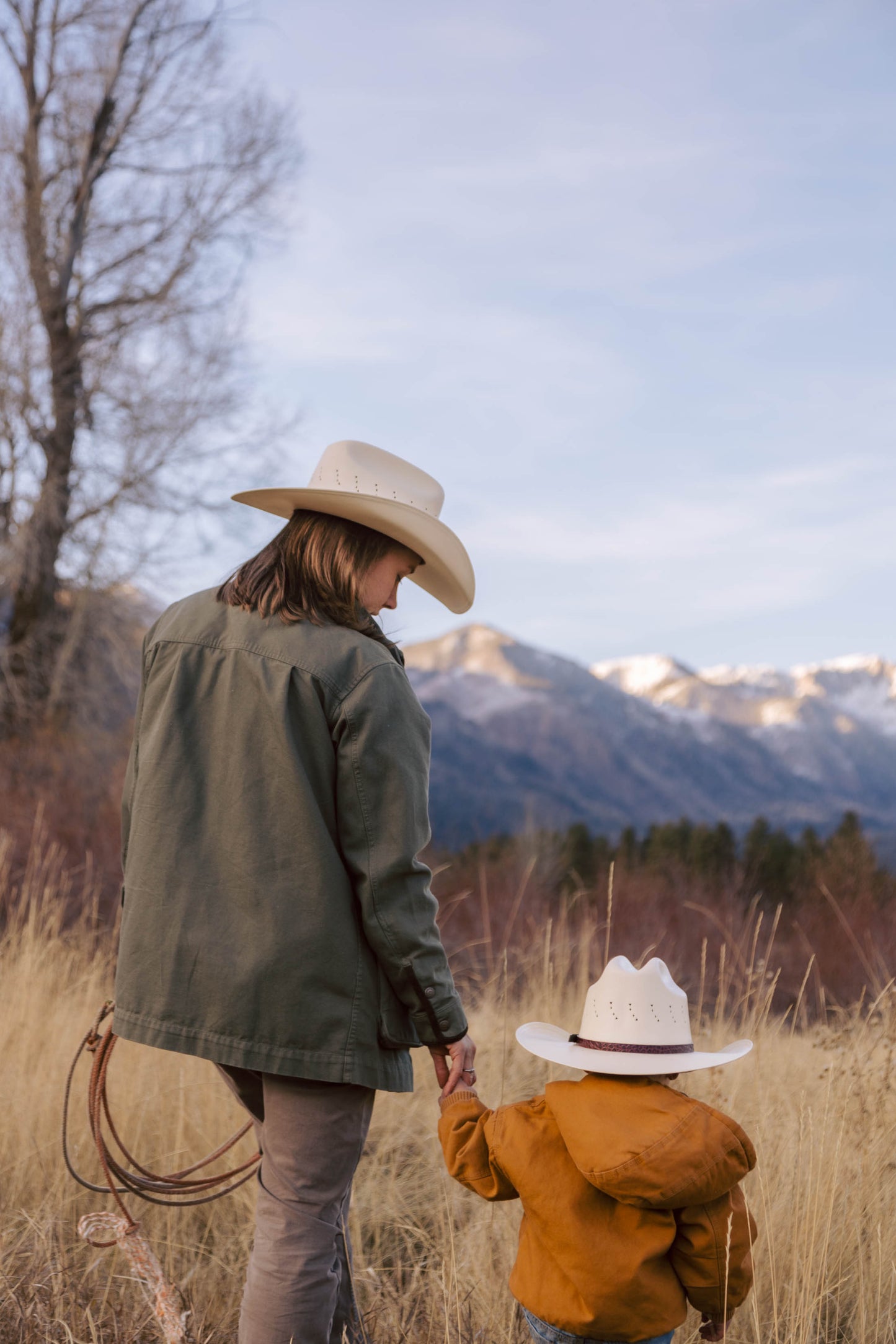 A woman and child wearing Turner Hat Cowboy Canvas cowboy hats standing in a field with mountains in the background